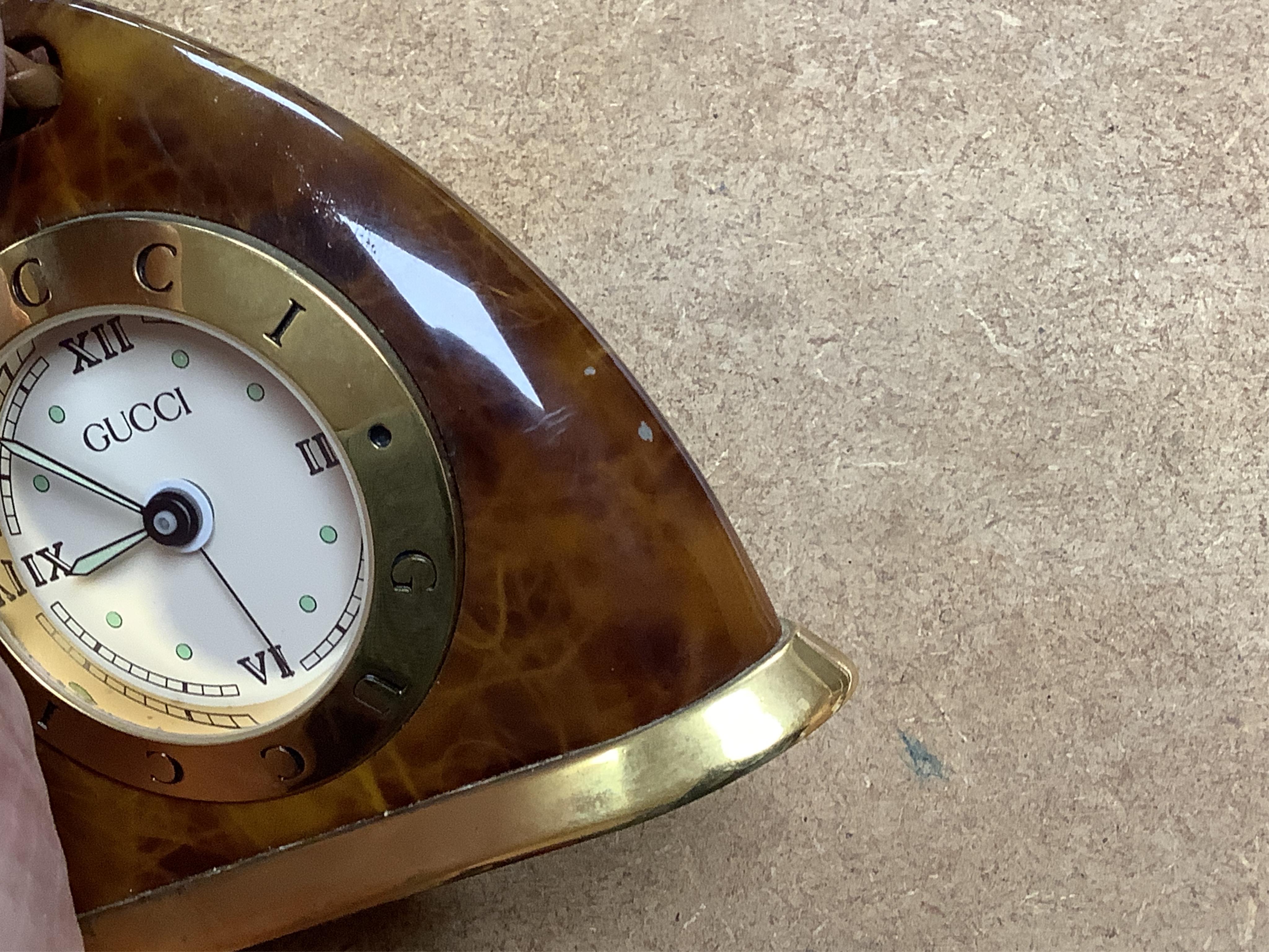 A Gucci gilt and enamelled stirrup shaped alarm clock with plaited and tasselled leather decoration, 9cm high